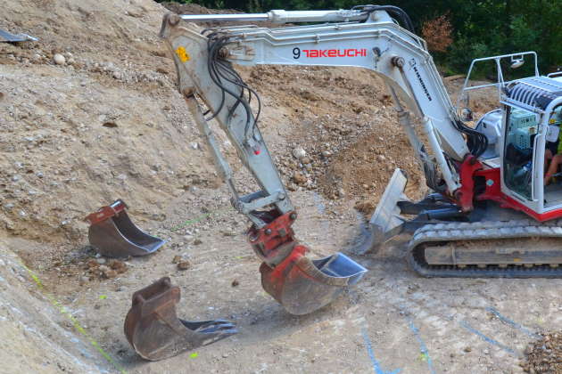 Raupenbagger mit verschiedenen Baggerlöffeln in Baugrube